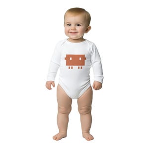Op de afbeelding: Een baby draagt een witte bodysuit met lange mouwen. De bodysuit heeft een gepixelde bruine afbeelding op de voorkant. De baby staat en glimlacht, tegen een witte achtergrond.