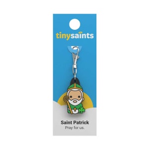 May include: A green and yellow Saint Patrick keychain with a silver clip. The keychain features a cartoon image of Saint Patrick holding a shamrock and a staff. The text "tiny saints" is printed on the card. The text "Saint Patrick Pray for us." is printed on the card.
