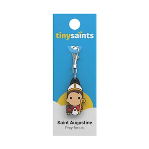 May include: A blue and yellow card with the text "tiny saints" on it. A small, cartoon-style figure of Saint Augustine is attached to the card with a silver clip. The figure is wearing a yellow and red robe and a mitre. The text "Saint Augustine Pray for us." is printed below the figure.