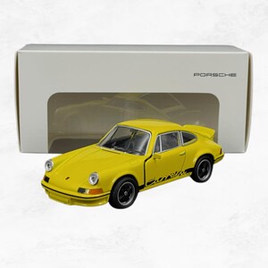 Peut inclure: Un modèle réduit de voiture de sport Porsche Carrera jaune avec des autocollants latéraux noirs, des phares ronds et des roues noires. La voiture est placée devant sa boîte d'emballage rectangulaire blanche d'origine portant le mot PORSCHE.