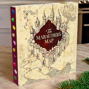 Op de afbeelding: Een doos met een gedetailleerde illustratie van Hogwarts Castle met de tekst "The Marauder's Map" in een bordeauxrode banner. De doos heeft een vintage perkamentachtige achtergrond en een rij kleurrijke jelly beans aan de zijkant.