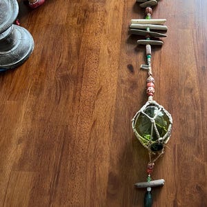 May include: A handmade driftwood mobile with a green glass float, white seashells, and colorful beads hanging from a wooden branch.
