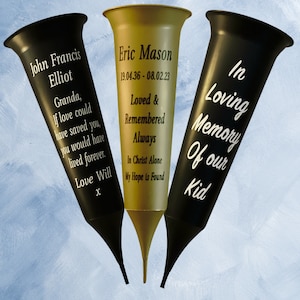 May include: Three black and gold flower vases with personalised messages. The vases are decorated with white text. The text on the vases reads: "John Francis Elliot", "Eric Mason 19.04.36-08.02.23 Loved & Remembered Always In Christ Alone My Hope is Found", and "In Loving Memory Of our Kid".