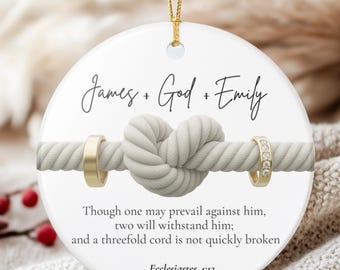 May include: A round white ceramic ornament featuring a central graphic of a thick rope tied in a knot with two gold rings on either side. The text reads James + God + Emily, followed by the Bible verse Ecclesiastes 4:12, hanging by a gold cord.
