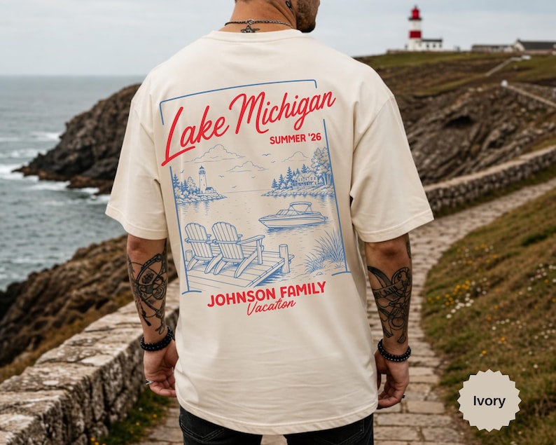 Puede incluir: Una camiseta de color marfil con un gr&aacute;fico azul y rojo en la espalda. El dise&ntilde;o incluye el texto Lake Michigan, Summer '26 y Johnson Family Vacation, con una ilustraci&oacute;n de dos sillas en un muelle, un barco y un faro.