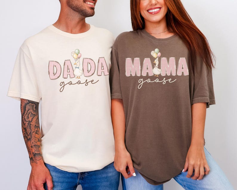 May include: A cream-colored t-shirt with the text DADA goose and a brown t-shirt with the text MAMA goose. Both shirts feature a graphic of a goose holding balloons, with the words DADA and MAMA in a pink plaid pattern and cursive text.