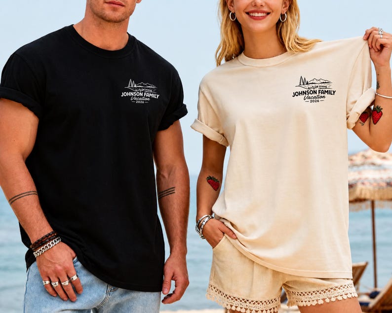 以下が含まれることがあります： 「Johnson Family Vacation 2026」の文字と山のグラフィックが入った黒とベージュのTシャツ。Tシャツは袖がまくられています。背景にはビーチの風景が写っています。
