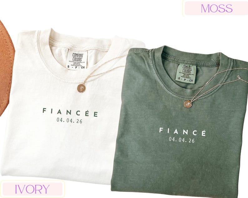 Puede incluir: Dos camisetas Comfort Colors, una marfil y otra verde musgo, con la palabra "FIANC&Eacute;E" y la fecha "04.04.26" impresas en la parte delantera. Cada camiseta tiene un collar con colgante dorado. Las camisetas son talla peque&ntilde;a.