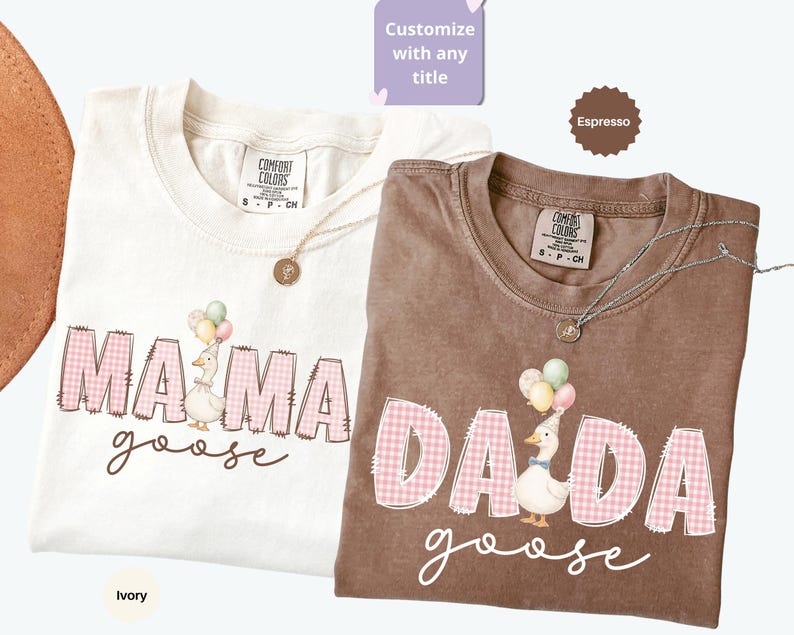 May include: Two short-sleeve t-shirts in ivory and espresso colors. The ivory shirt features the text MAMA goose with a goose wearing a party hat and balloons. The espresso shirt features the text DADA goose with a goose wearing a party hat and balloons. Both shirts have pink gingham lettering.