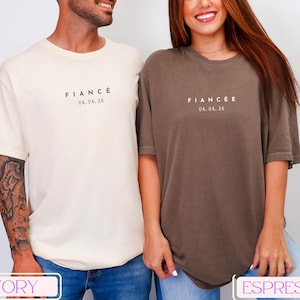 Puede incluir: Dos camisetas de manga corta, una marfil y otra espresso, cada una con la palabra "FIANC&Eacute;" o "FIANC&Eacute;E" y la fecha 04.04.26 impresa en la parte delantera. Las camisetas son de corte holgado, adecuadas para parejas.