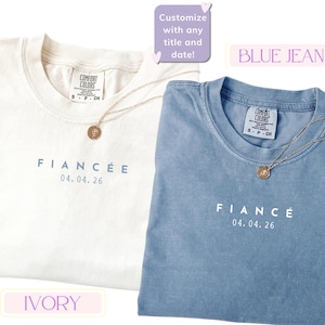 Puede incluir: Se muestran dos camisetas, una marfil y otra azul. La camiseta marfil dice "FIANC&Eacute;E" y la camiseta azul dice "FIANC&Eacute;", ambas con una fecha. Cada camiseta tiene un collar dorado. Tambi&eacute;n se ve el texto "&iexcl;Personaliza con cualquier t&iacute;tulo y fecha!"