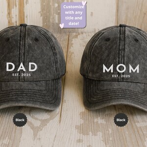 May include: Two black baseball caps with white text. One cap says "DAD EST. 2025" and the other says "MOM EST. 2025". The caps have a distressed look and a curved brim. The text "Customize with any title and date!" is also visible.