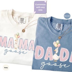 May include: Two short-sleeved t-shirts in ivory and blue jean colors. The ivory shirt features the text MAMA in pink gingham with a goose wearing balloons. The blue shirt features the text DADA in pink gingham with a goose wearing balloons.