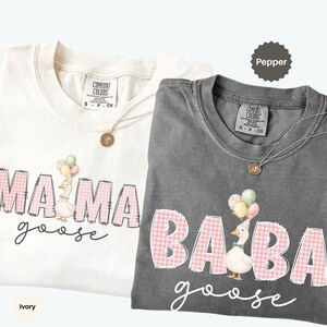 May include: Two t-shirts, one ivory and one pepper gray, featuring a graphic print. The ivory shirt displays the text MAMA goose with a goose holding balloons. The pepper shirt displays the text BABA goose with a goose holding balloons.