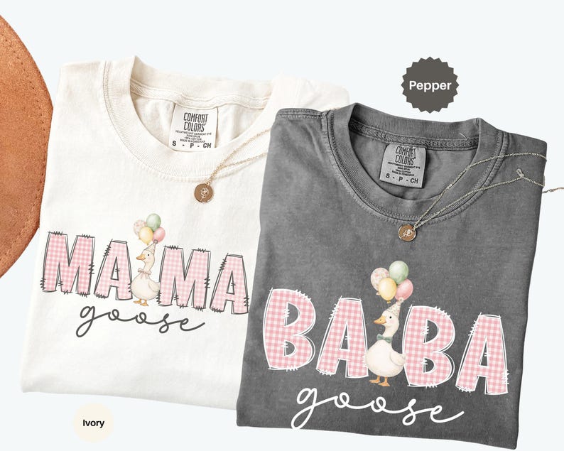 May include: Two t-shirts, one ivory and one pepper gray, featuring a graphic print. The ivory shirt displays the text MAMA goose with a goose holding balloons. The pepper shirt displays the text BABA goose with a goose holding balloons.