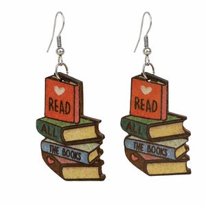 May include: A pair of wooden earrings shaped like stacks of books. Each earring features a red book on top with the word "READ" and a heart. Below are books with the words "ALL" and "THE BOOKS". The earrings have silver-colored hooks.