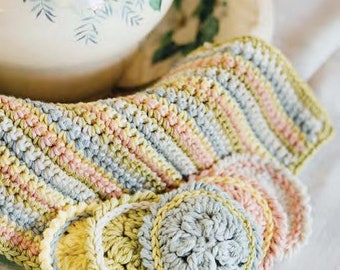Peut inclure: Un torchon en crochet avec un motif rayé dans les tons de rose, bleu et jaune. Le torchon a un motif floral décoratif au centre.