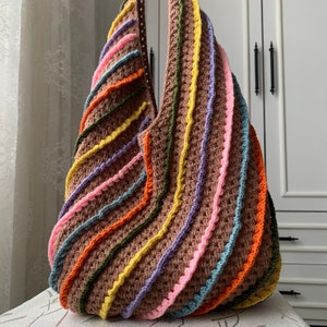 May include: A large, crocheted tote bag with a brown base and colourful stripes of pink, orange, yellow, green, and blue.