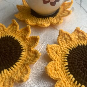 May include: Three crocheted sunflower coasters in yellow and brown. The coasters are made with a detailed stitch pattern and have a raised center.