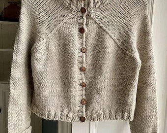 May include: A beige knitted cardigan with a high collar and button closure. The cardigan has a textured knit pattern and a slightly cropped length.