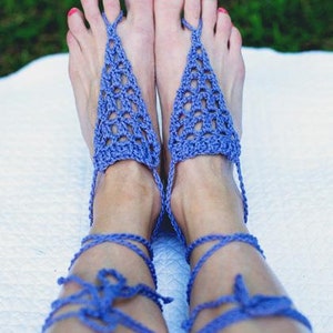 Puede incluir: Sandalias descalzas de ganchillo azul. Las sandalias tienen un diseño triangular sobre el pie y se atan alrededor del tobillo. La imagen muestra las sandalias en los pies de una persona con esmalte de uñas rosa. Un accesorio de verano.