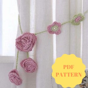 May include: A crochet garland with pink and green flowers. The garland is hanging on a white curtain. The text "PDF PATTERN" is on a yellow circle.