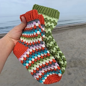 May include: Two crocheted socks, one in a green and white pattern and the other in a multi-colored pattern with orange, green, white, blue, and purple.