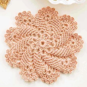 May include: A delicate, crocheted doily in a soft peach colour. The doily features a circular design with intricate floral patterns.