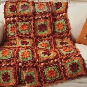 May include: A crocheted throw blanket with a patchwork design featuring squares of green, orange, and red yarn. The blanket is made with a floral motif and has a fringed edge.