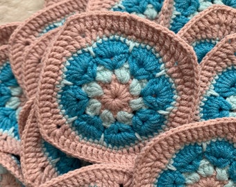 May include: Close-up of a crocheted blanket made of pink and blue squares. The squares have a floral pattern in the center.