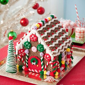 May include: A crocheted gingerbread house decorated with candy canes, gumdrops, and sprinkles. The house is sitting on a silver tray and surrounded by candy.