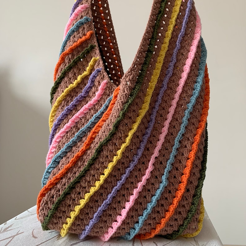 May include: A brown crocheted tote bag with diagonal stripes of pink, orange, yellow, green, and blue yarn.