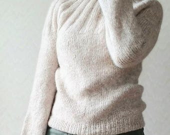 May include: A soft, light beige sweater with a high neck and long sleeves. The sweater has a textured knit and a relaxed fit.