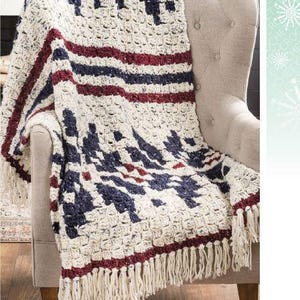 Può includere: Una coperta all'uncinetto con un motivo geometrico in tonalità di bianco, rosso e blu. La coperta ha un bordo a frangia ed è drappeggiata su una sedia.