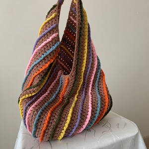 May include: A large, crocheted tote bag with a brown base and colourful stripes of pink, yellow, orange, blue, and purple.