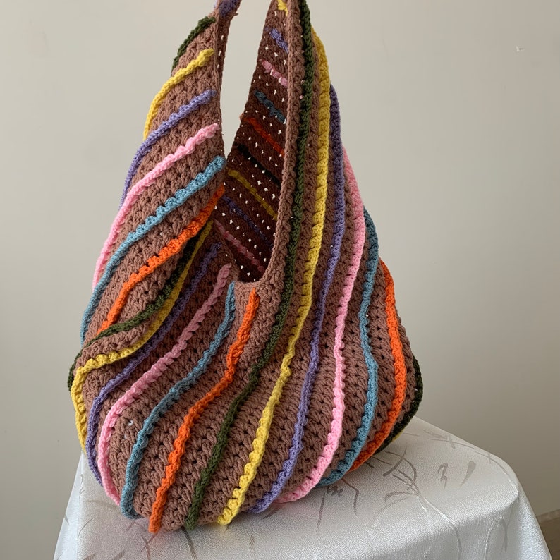 May include: A large, crocheted tote bag with a brown base and colourful stripes of pink, yellow, orange, blue, and purple.