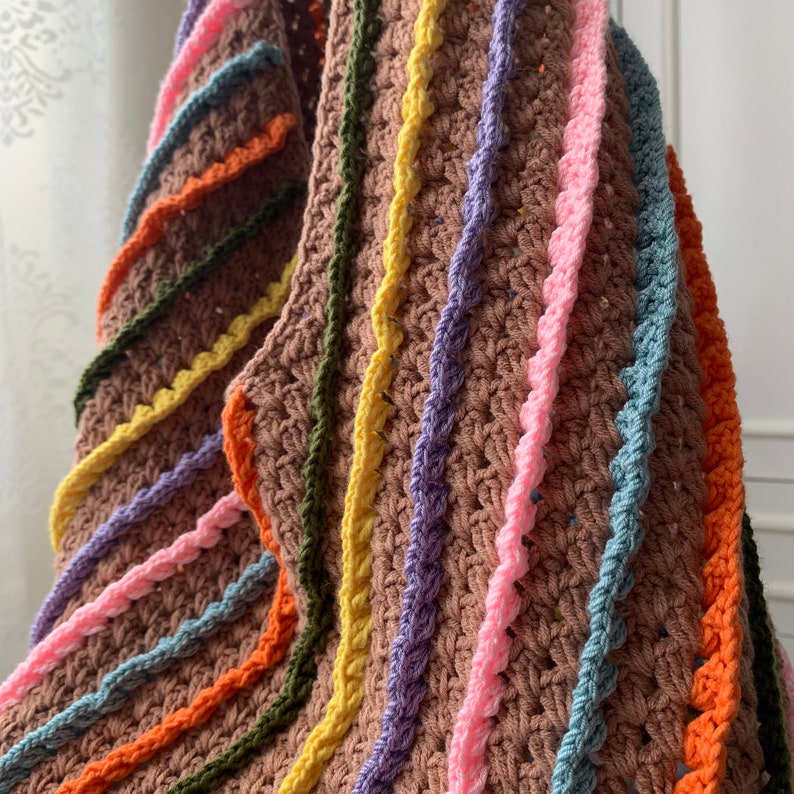 May include: A brown crocheted throw blanket with colourful stripes in shades of orange, yellow, green, blue, and pink.