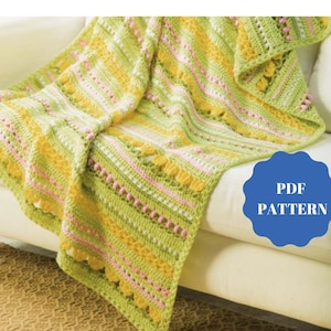 May include: A handmade crochet blanket in shades of green, yellow, and pink, draped over a white sofa. The blanket features a striped pattern with scalloped edges and the text "PDF PATTERN" on a blue badge.