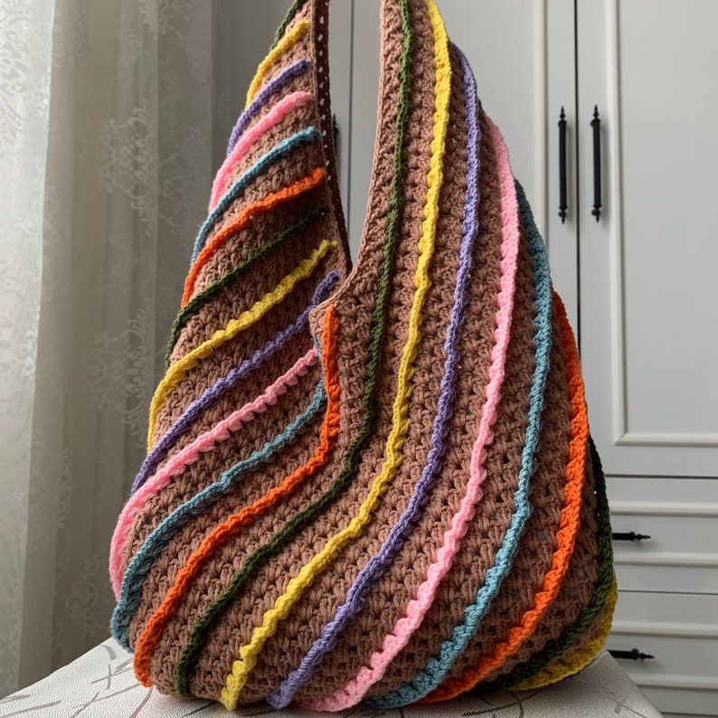 May include: A large, crocheted tote bag with a rainbow stripe pattern. The bag is made of brown, pink, yellow, orange, and blue yarn.