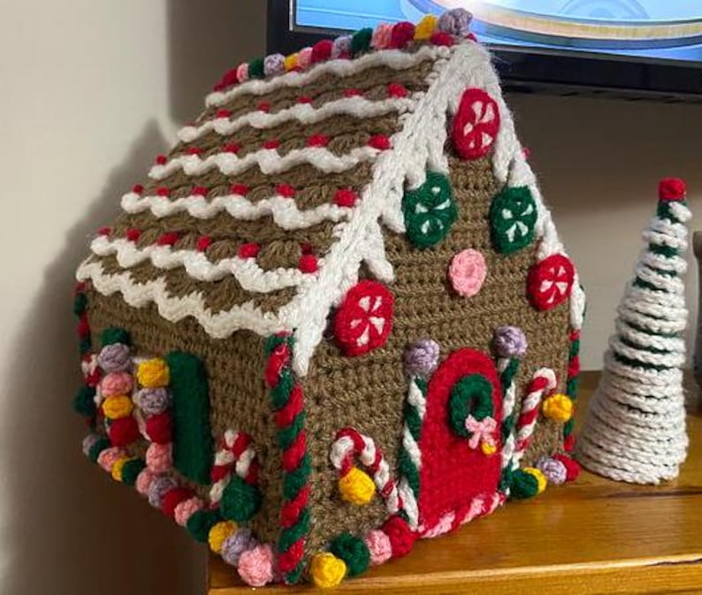 May include: A crocheted gingerbread house with white frosting, red candy canes, and colorful sprinkles. The house has a green door and a red roof.