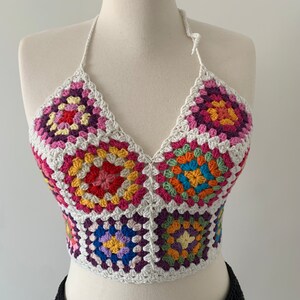 May include: A colorful crochet halter top with a white background and a geometric pattern. The top is made of yarn in shades of pink, red, orange, yellow, green, blue, and purple.