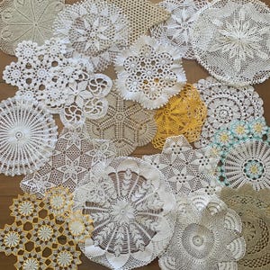 May include: A collection of various round and square crochet doilies in white, cream, beige, and yellow. The pieces feature intricate openwork patterns, floral motifs, and scalloped edges, showcasing diverse needlework techniques and thread textures.