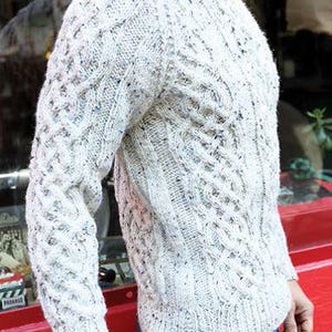 May include: A white cable knit sweater with a speckled pattern. The sweater has a crew neck and long sleeves.