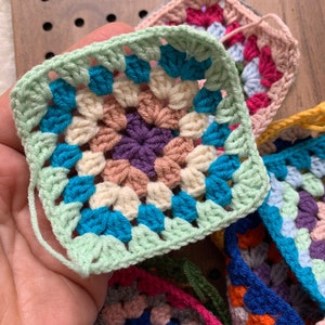 Peut inclure: Un ensemble de carrés de grand-mère au crochet de différentes couleurs, notamment le vert, le bleu, le rose, le violet et le jaune.