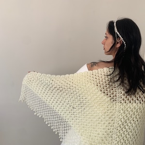 May include: A white crocheted shawl with a delicate lace trim. The shawl is draped over a person's shoulders and is made with a fine, open stitch.