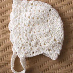 Puede incluir: Gorrito de bebé blanco de ganchillo con borde festoneado y una cinta.