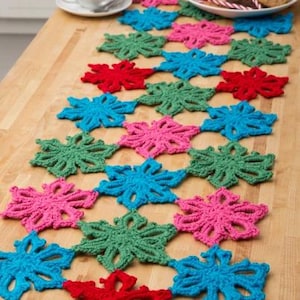 Könnte beinhalten: Handgefertigter gehäkelter Tischläufer mit Schneeflockenmuster. Der Läufer ist aus verschiedenen Farben gefertigt, darunter Rot, Grün, Blau und Rosa. Der Tischläufer ist etwa 152 cm lang.