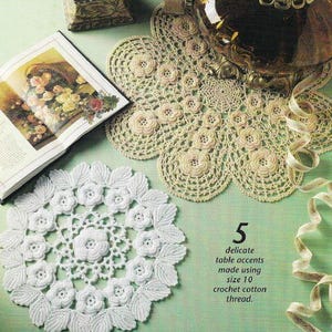 Op de afbeelding: Handgemaakte gehaakte tafelaccessoires in crème en wit. De afbeelding toont een witte doily met bloempatronen en een crèmekleurige doily met een geschulpte rand. De tekst luidt: "5 delicate tafelaccenten gemaakt met maat 10 haakkatoen."