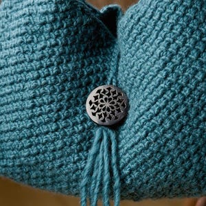 May include: A teal crocheted bag with a decorative wooden button and a tassel. The bag is made with a textured stitch.