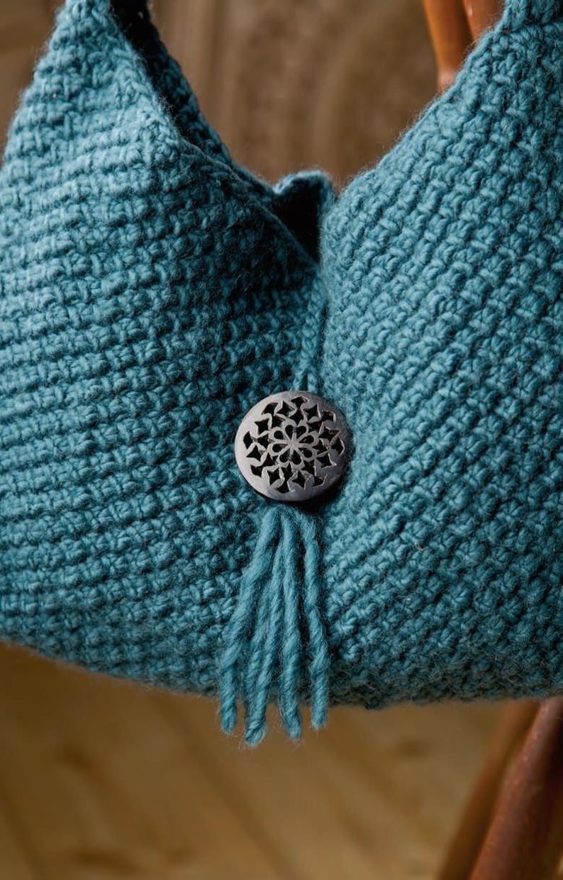 May include: A teal crocheted bag with a decorative wooden button and a tassel. The bag is made with a textured stitch.